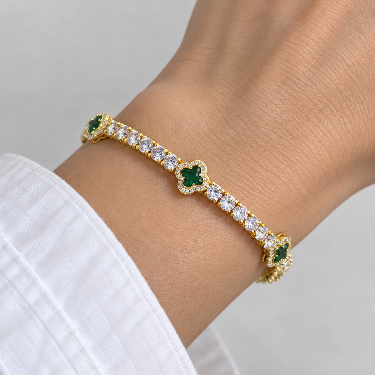 Ice63 Clover Tennis Chain Braceletの着用イメージ。白い袖の手首にゴールドカラーとグリーンのクローバーブレスレット